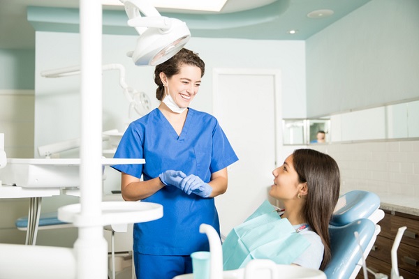 Smiling female dentist in uniform talking to teenage girl at dental clinic