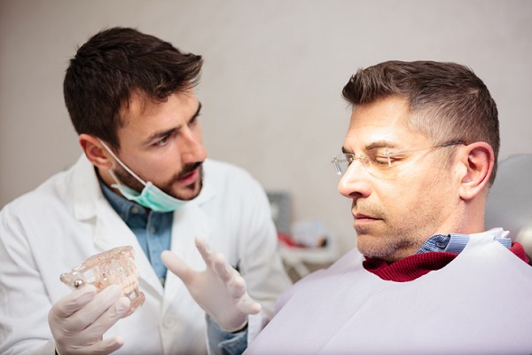 Young male dentist and mature patient discussing dentures during exam in a dental clinic