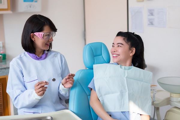 Asian woman dentist smiling and holding a dental tool and female patients lying in the dental chair in a hospital.